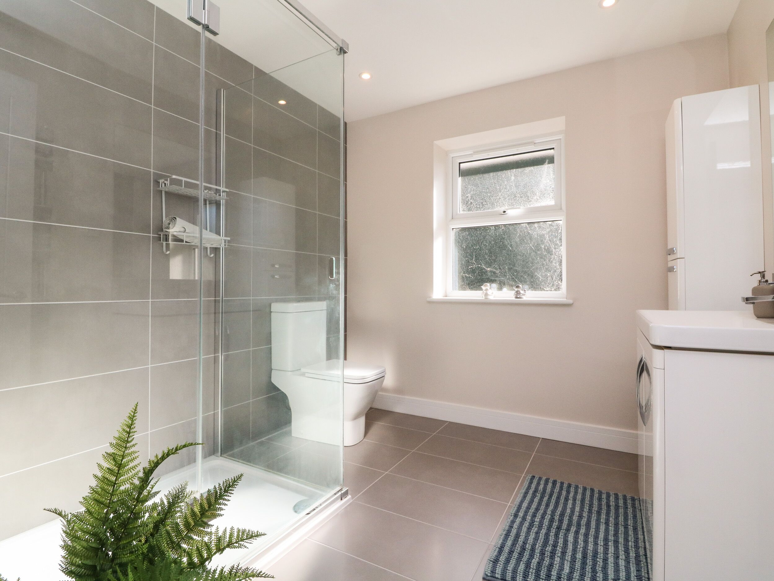 Un baño moderno con cabina de ducha de vidrio, inodoro, ventana con vistas y lavamanos.