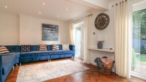 A living room with a blue sofa, a large abstract painting, a wooden herringbone floor, and a view of the outdoors through a sliding glass door. - 4 Woodland Park (Bideford)
