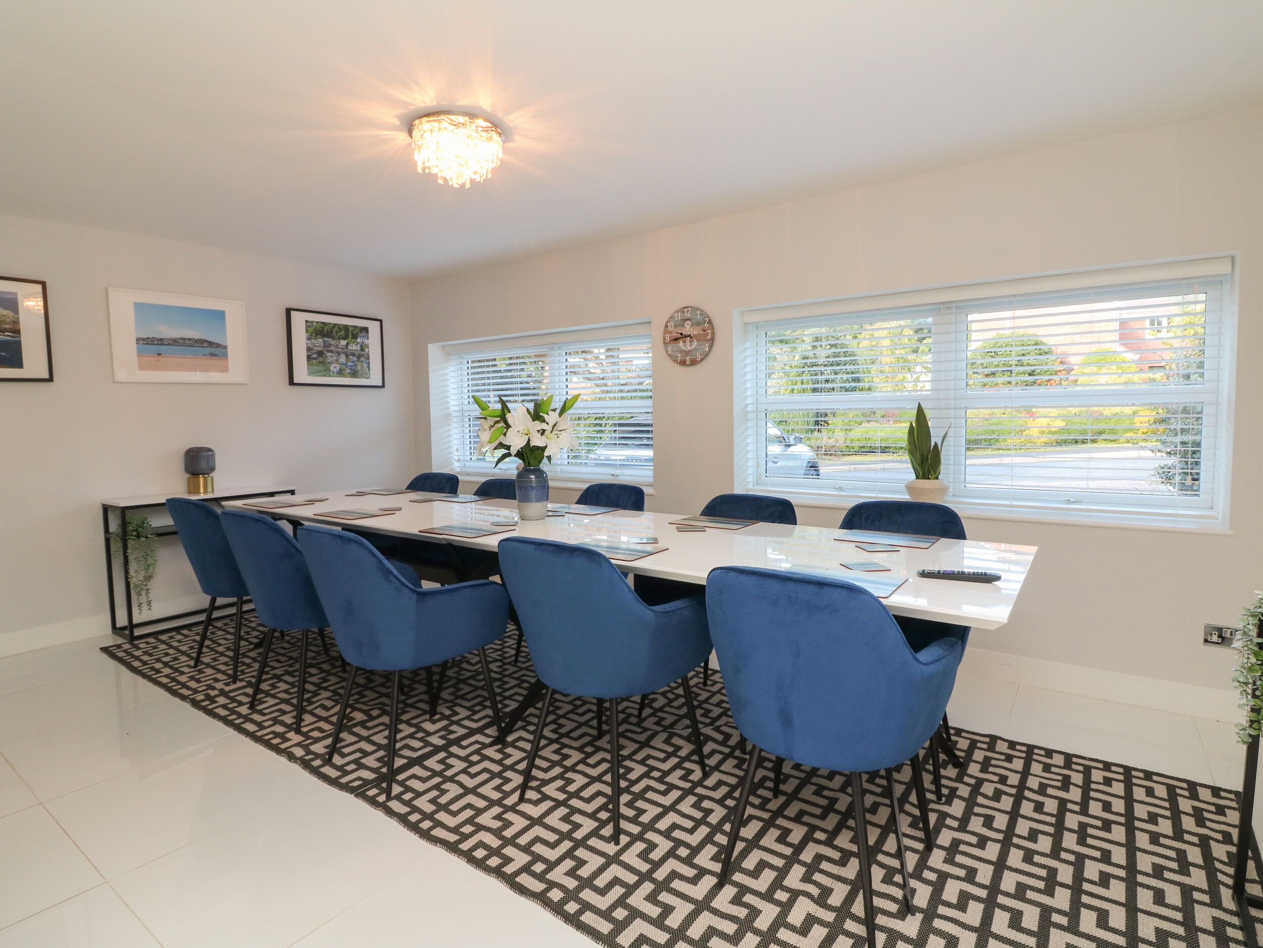 A dining area with a long table, blue chairs, a vase with flowers, and a chandelier.