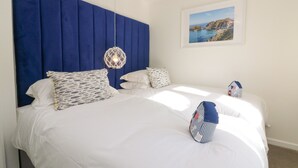 A bedroom with a large bed, a blue headboard, and a hanging light fixture. - 4 Woodland Park (Bideford)