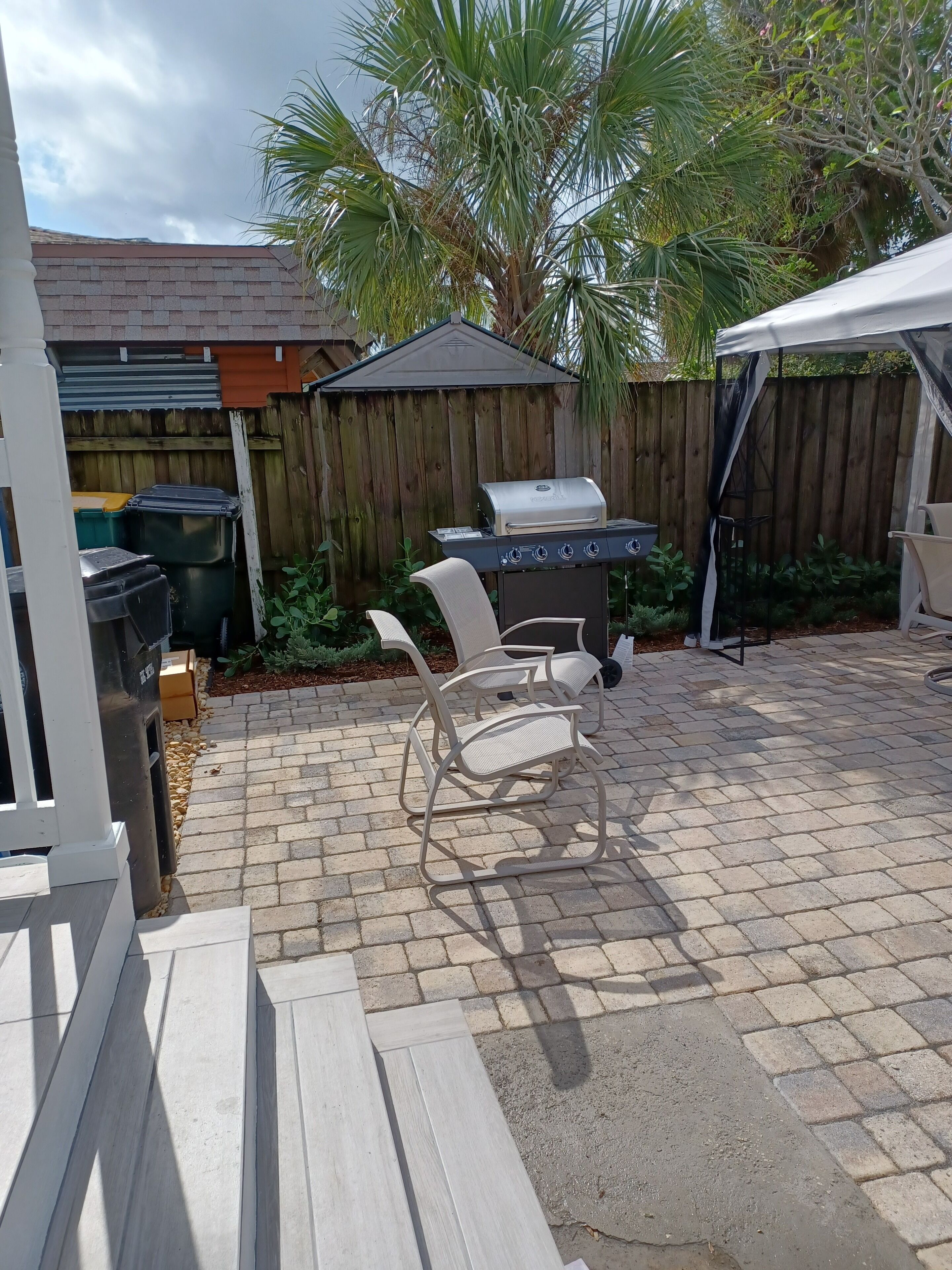 Een terras met een barbecue, tuinmeubilair en een houten omheining.