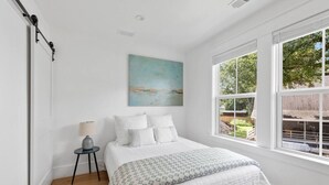 A bedroom with a bed, a painting, a lamp, and a window with a view of the outdoors.
