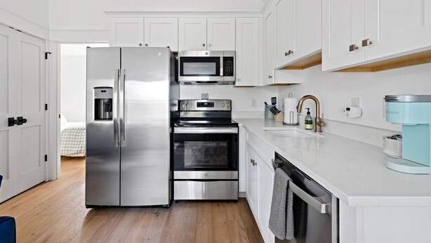 A modern kitchen with stainless steel appliances, white cabinetry, and a wooden floor.