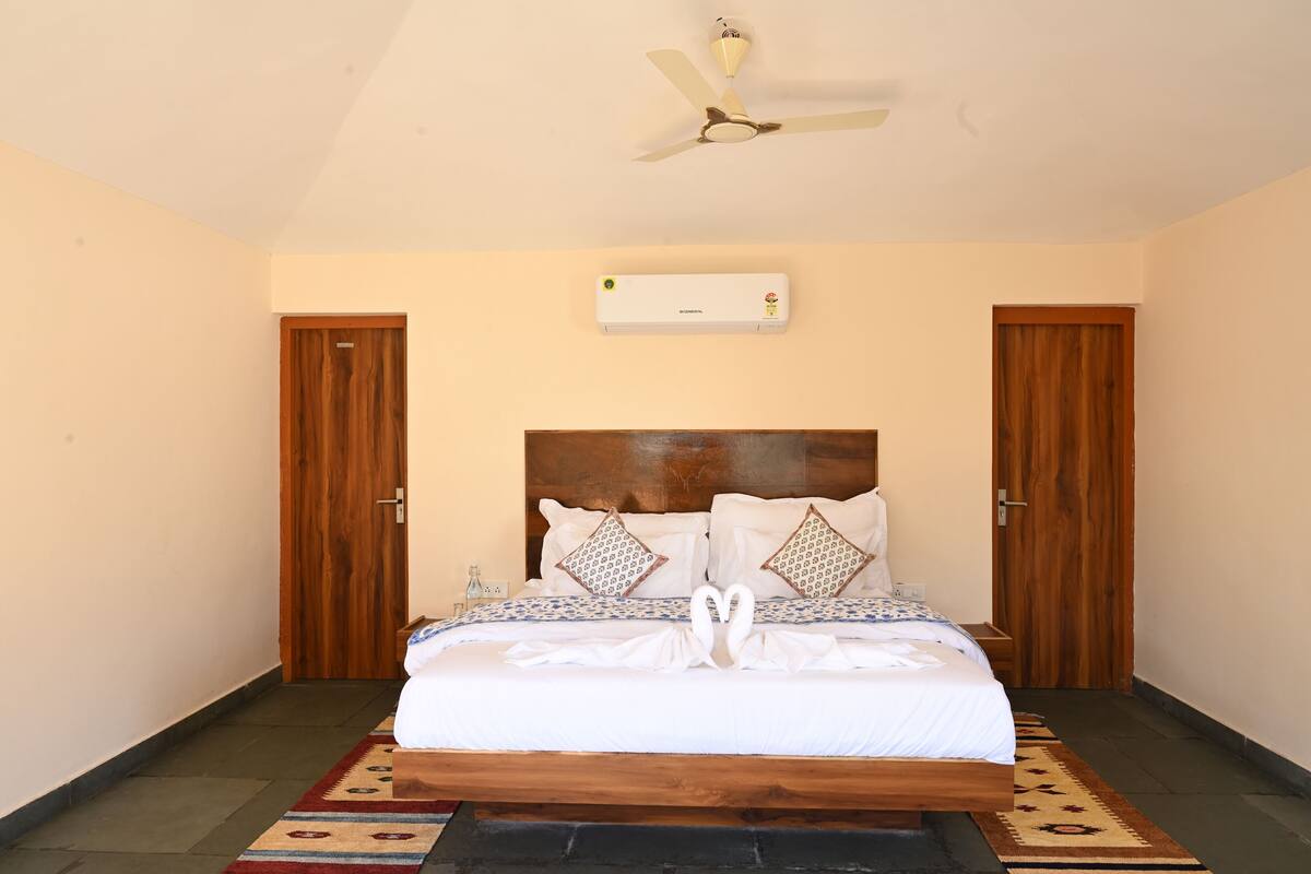 A bedroom with a bed, a ceiling fan, an air conditioning unit, and two wooden doors.