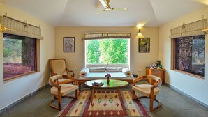 Una habitación acogedora con una mesa redonda, dos sillas de madera, un sofá con cojines y un ventanal con vistas al verdor.