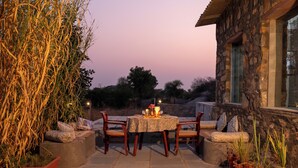 Un patio al aire libre con una mesa y sillas de piedra, rodeado de macetas con plantas y un muro de piedra.
