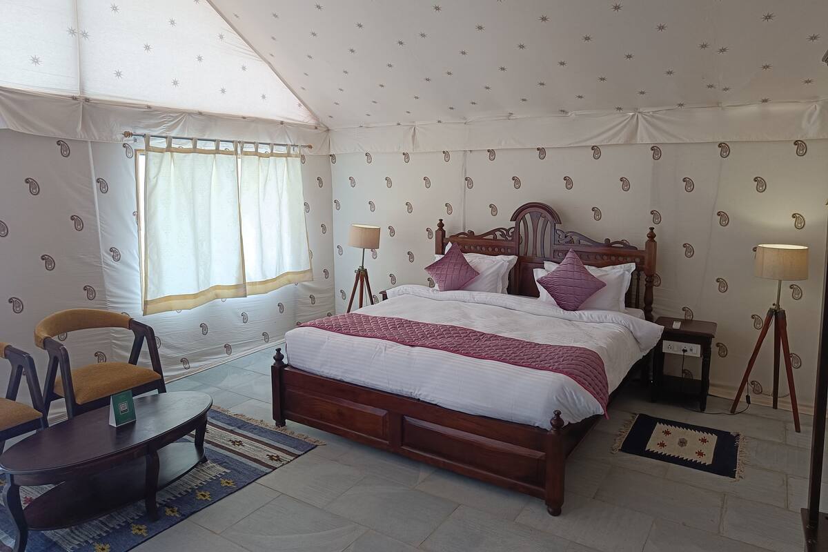 A bedroom with a bed, two bedside lamps, a chair, a small table, and a window with curtains.