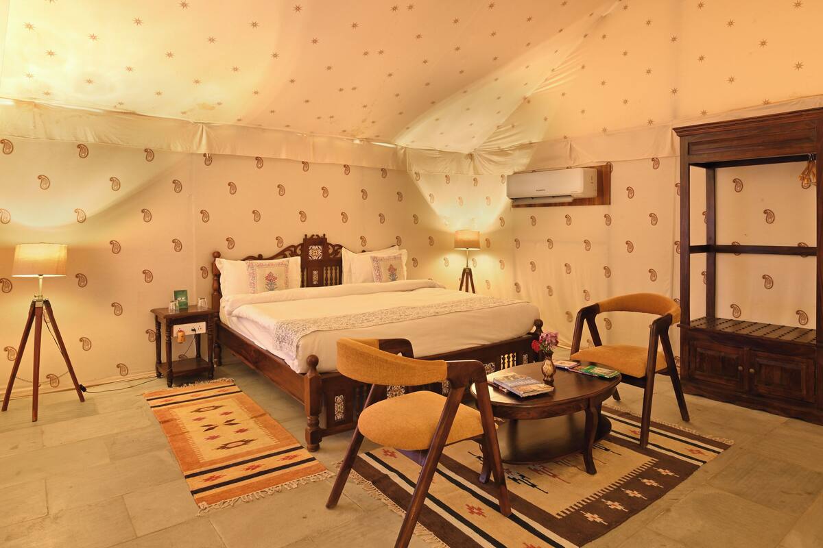 A bedroom with a bed, two chairs, a small table, a lamp, and a nightstand.
