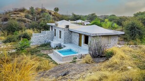 Una casa de piedra con piscina, rodeada de hierba seca y arbustos.