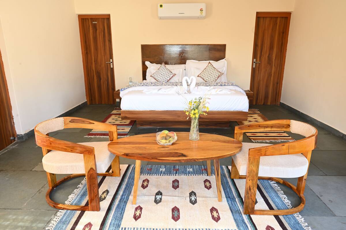 A bedroom with a bed, two wooden chairs, a round wooden table, and a patterned rug.