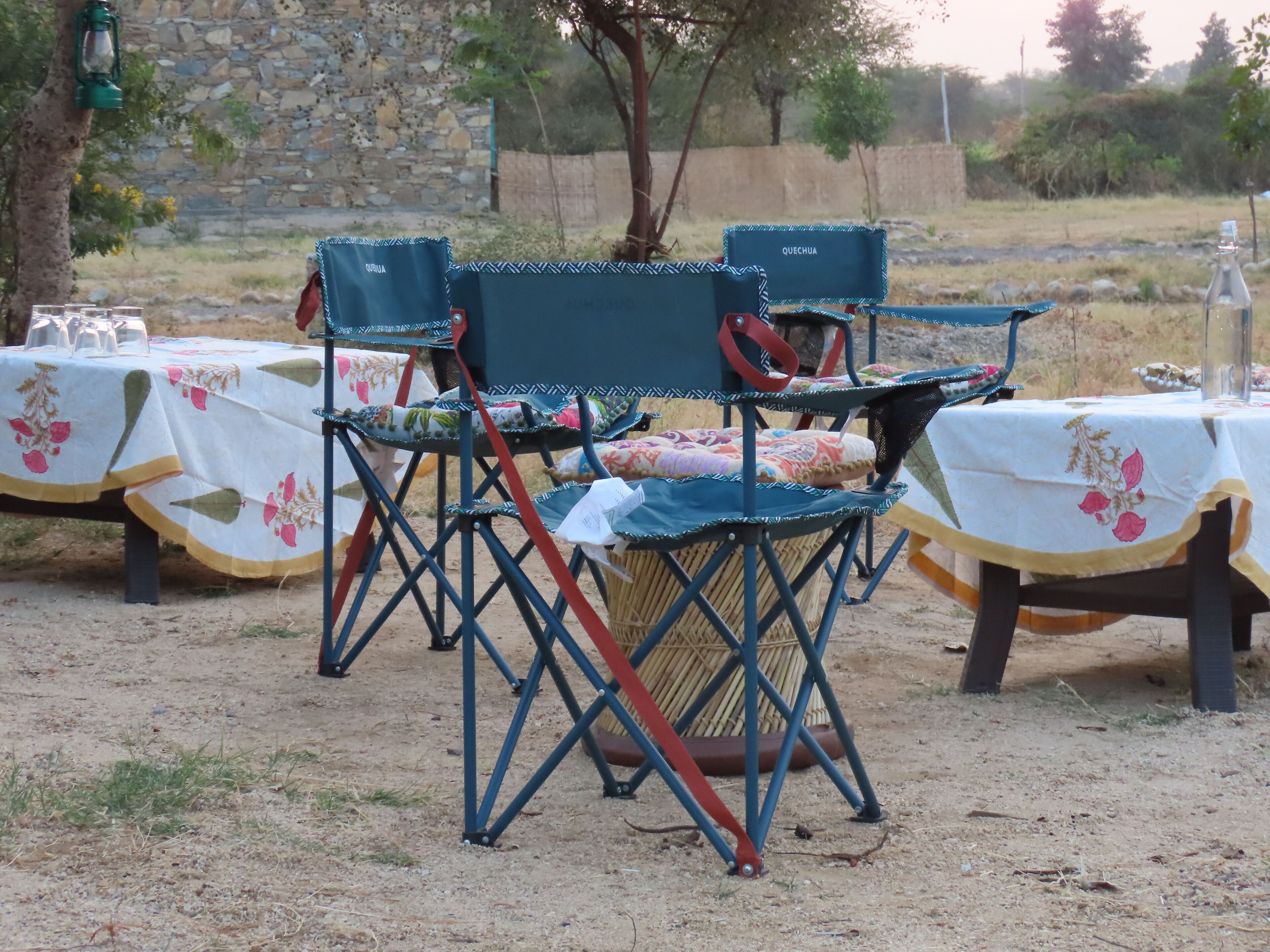 Sillas para comedor al aire libre con manteles florales, un muro de piedra y un árbol de fondo.