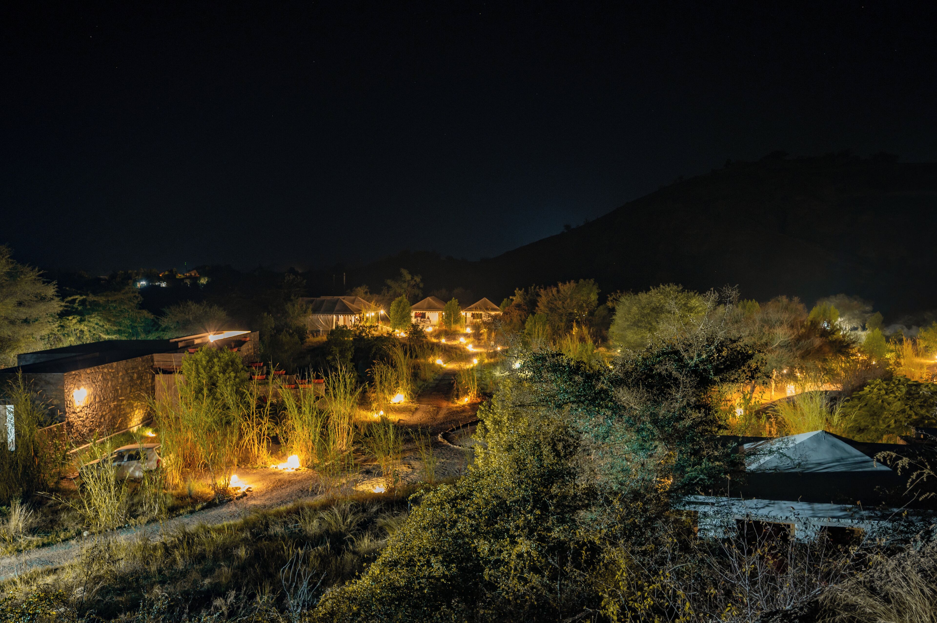 A nighttime view of a rural area with several buildings, including a house with a lit roof and a barn.