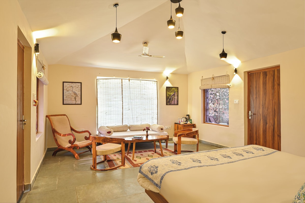 A bedroom with a bed, a wooden chair, a sofa, a table, and a window with blinds.