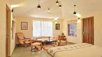A bedroom with a bed, a wooden chair, a sofa, a table, and a window with blinds.