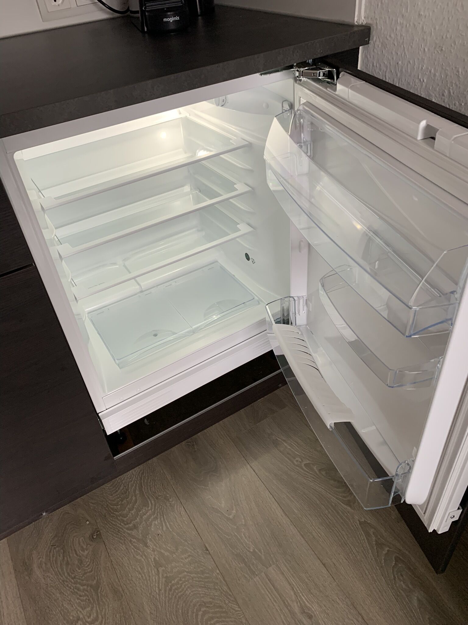 Ein offener Kühlschrank mit klaren Regalen und einer schwarzen Arbeitsplatte.