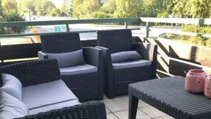 A patio area with wicker furniture, including two chairs and a table, and a pink vase on the table. - Modern apartment, right on a lake in Winterberg-Niedersfeld (Winterberg)
