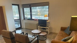 A modern living room with a sofa, chairs, a coffee table, a TV, and a radiator. - Modern apartment, right on a lake in Winterberg-Niedersfeld (Winterberg)