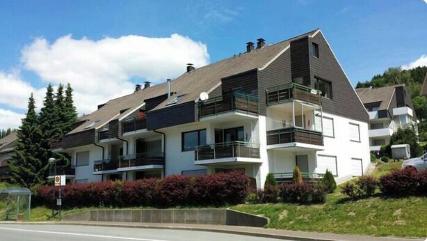 A modern multi-story residential building with balconies, a sloped roof, and a landscaped front yard. - Modern apartment, right on a lake in Winterberg-Niedersfeld (Winterberg)