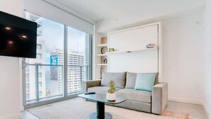 A modern living room with a sofa, a coffee table, and a TV mounted on the wall. - Modern & newly built studio Pool|Gym|Restaurant| (Miami)