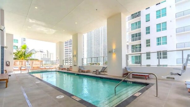 An indoor swimming pool with lounge chairs and a view of a tall building. - Modern & newly built studio Pool|Gym|Restaurant| (Miami)