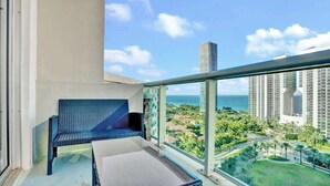 Een balkon met een blauwe geweven stoel, een tafeltje en uitzicht op een stadsbeeld en de oceaan.