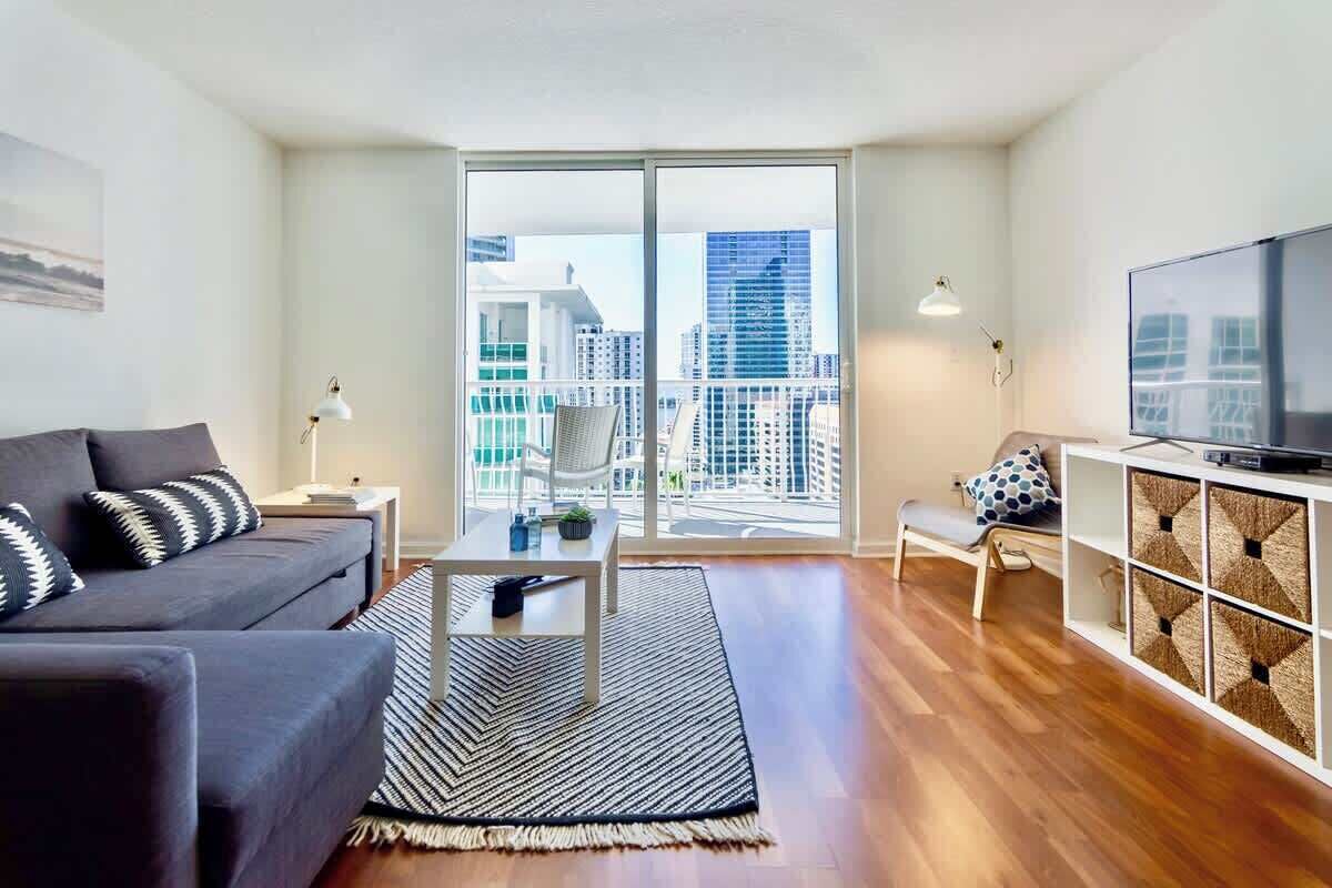 A modern living room with a sofa, a coffee table, a TV, and a balcony with a city view.