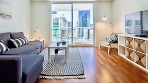 A modern living room with a sofa, a coffee table, a TV, and a balcony with a city view. - Ocean & City Views Lux Miami Brickell | Sleeps 5 (Miami)