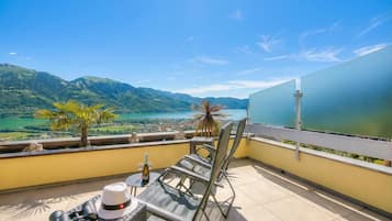 A balcony with a view of mountains and a lake, a table with a bottle, binoculars, and a hat.