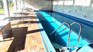 Una piscina con paredes de azulejos y una zona de terraza soleada con sillas de descanso.