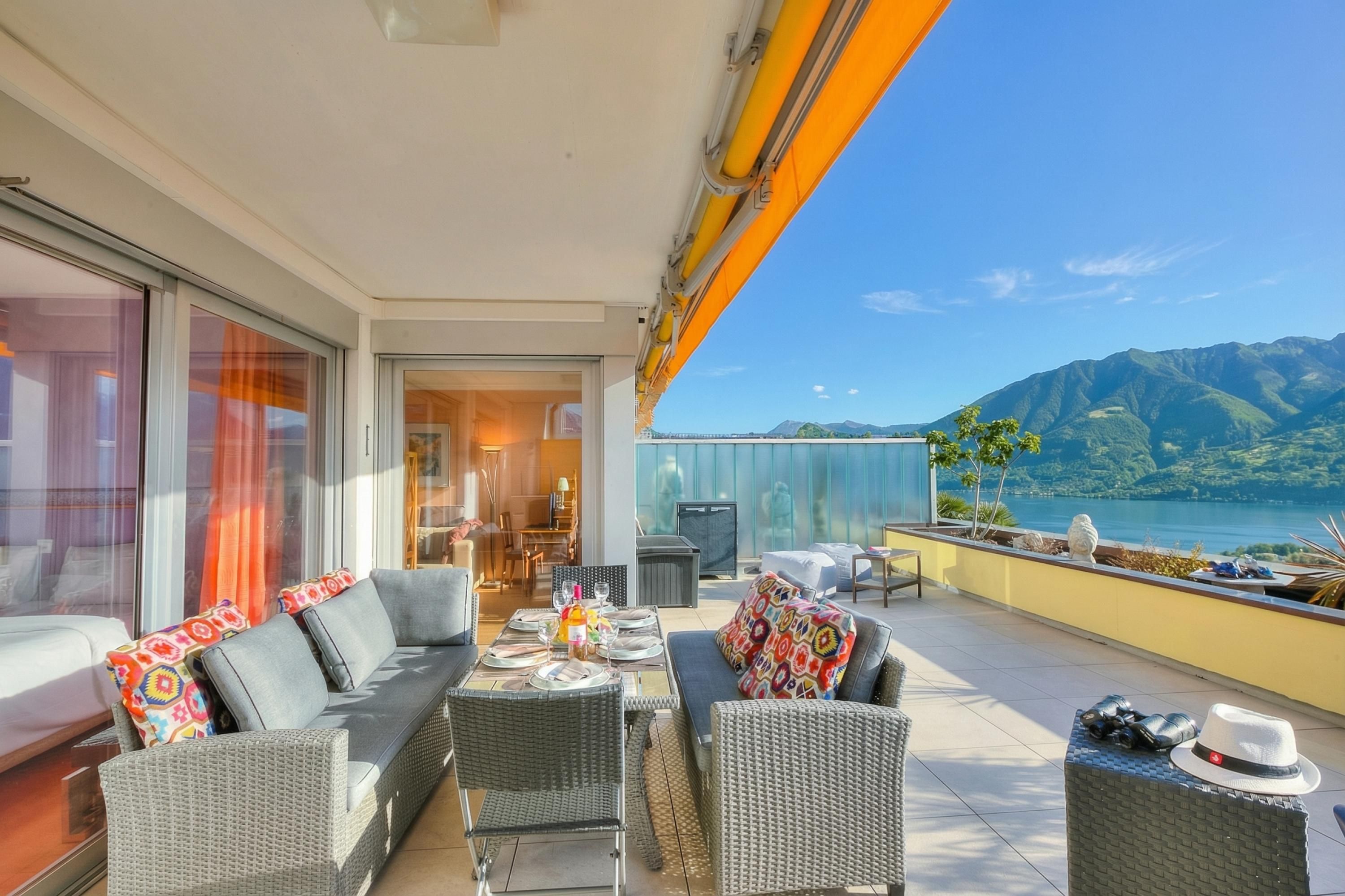 A balcony with outdoor furniture, a dining table set, and a view of mountains and water.