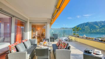 A balcony with outdoor furniture, a dining table set, and a view of mountains and water.