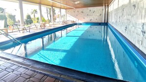 An indoor swimming pool with clear blue water, surrounded by lounge chairs and a tiled wall. - Panorama maggiore apartment (Locarno)