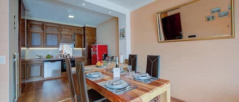 A dining area with a wooden table set for four, a kitchen in the background, and a large mirror on the wall.