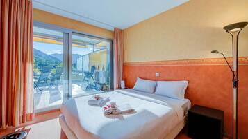 A hotel room with a bed, a nightstand, a lamp, a window with curtains, and a view of the outdoors.