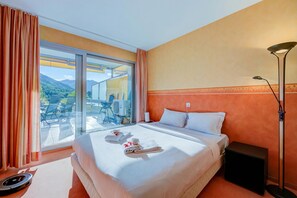 A hotel room with a bed, a nightstand, a lamp, a window with curtains, and a view of the outdoors. - Panorama maggiore apartment (Locarno)