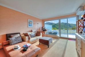 Una sala de estar moderna con un sofá, un reposapiés y un comedor con vistas a las montañas.