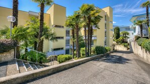 A multi-story building with a central staircase, surrounded by palm trees and greenery. - Panorama maggiore apartment (Locarno)