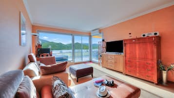 Un salón espacioso con un ventanal grande, televisor, aparador de madera y sofá.