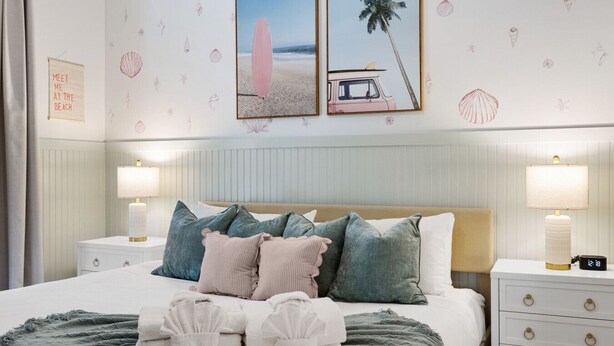 A neatly arranged bedroom with a bed, pillows, a bedside table, and a nightstand. - Folly - Large Front Porches - One Block to Beach (Folly Beach)