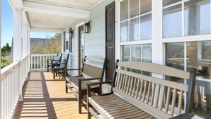A covered porch with wooden benches and a table, large windows, and a view of the outdoors. - Folly - Large Front Porches - One Block to Beach (Folly Beach)