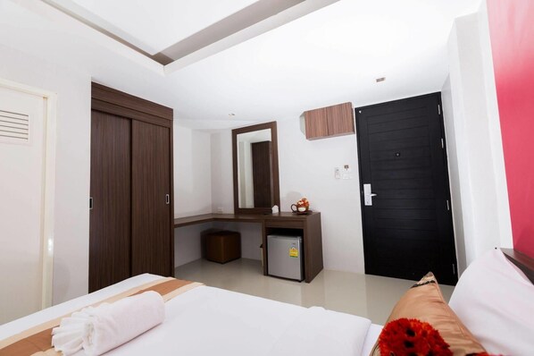Une chambre d’hôtel moderne équipée d’un lit, d’un bureau avec un miroir, d’un petit réfrigérateur et d’une porte noire.