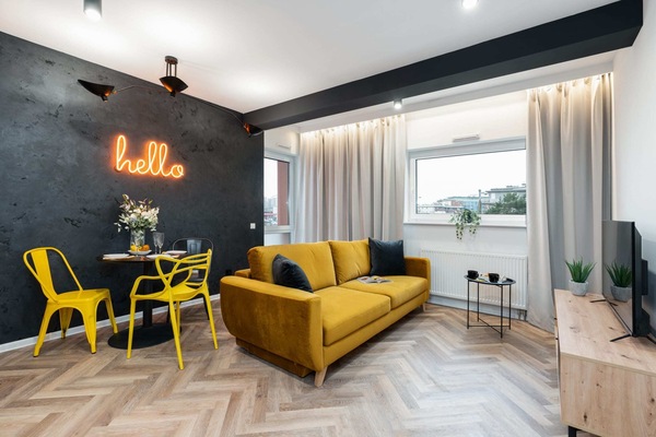 A modern living room with a mustard-yellow sofa, a round table, and a "hello" neon sign on the wall.