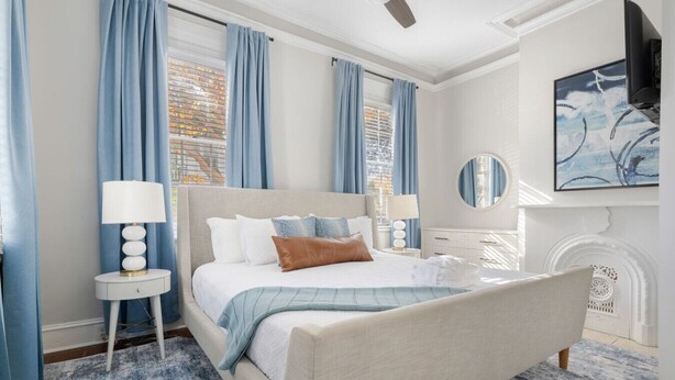Una camera da letto con un letto, due comodini, uno specchio rotondo, un camino e una ventola a soffitto.