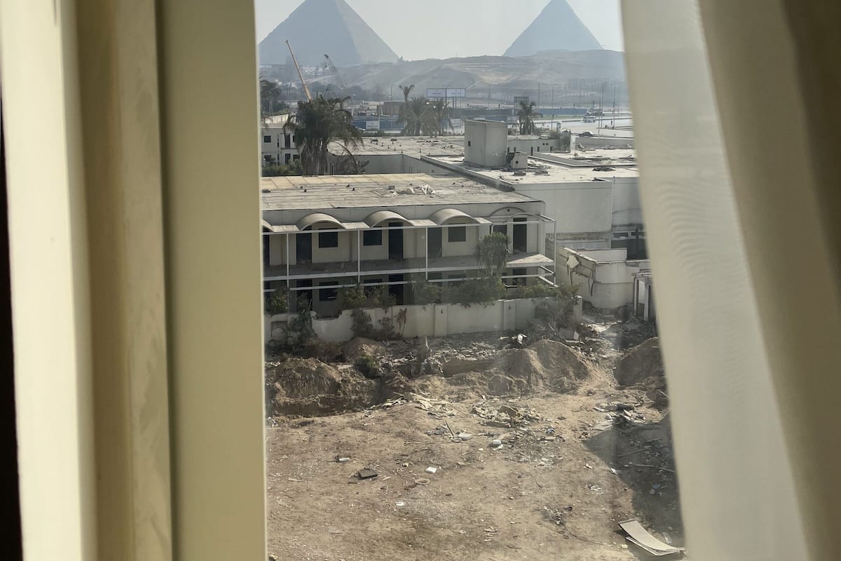A view through a window of a building with two pyramids in the background, construction sites, and a clear sky.