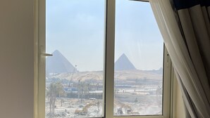 Una habitación con ventana que da a una obra en construcción y pirámides al fondo.