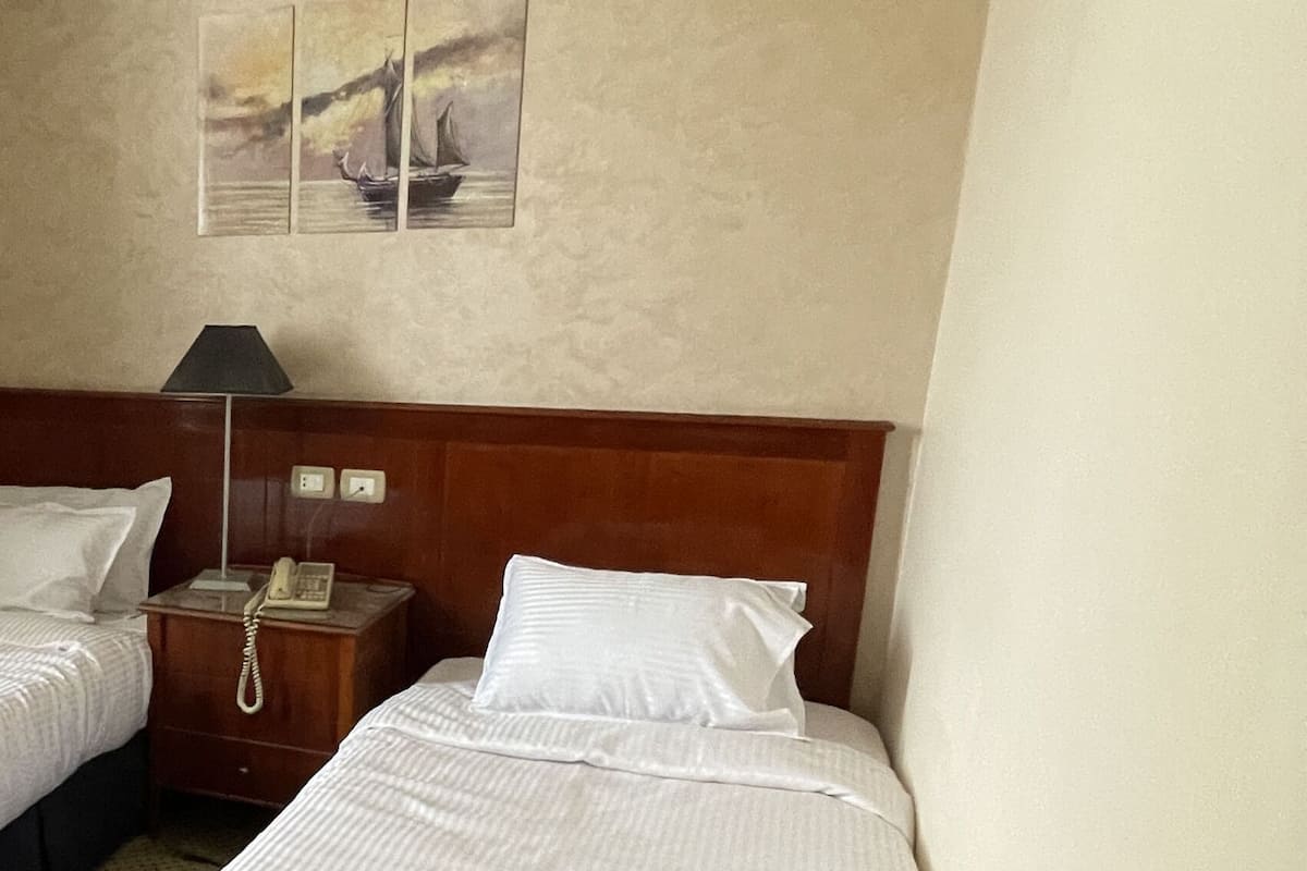 A hotel room with two beds, a wooden headboard, a wall-mounted air conditioner, and a telephone on a wooden nightstand.