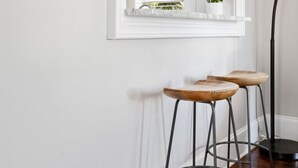 En hall med en inramad karta, ett fönster med persienner, en växt och två pallar.