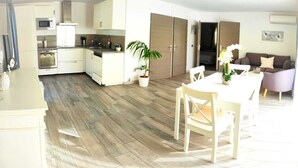 A modern kitchen with white cabinets, a microwave, and an oven. There is a dining area with a white table and chairs, and a potted plant. - Escape near the sea (La Ciotat)