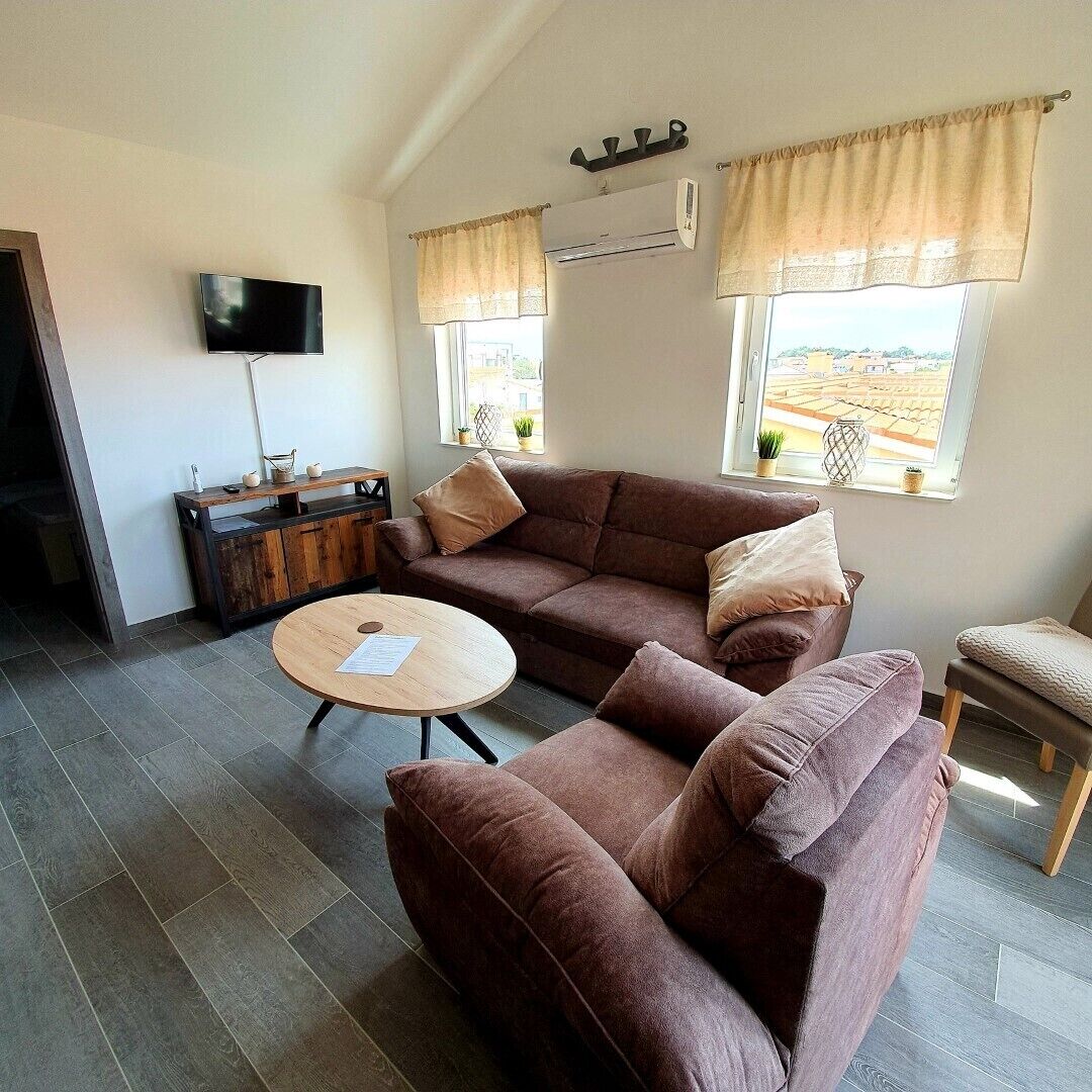 A living room with a brown sofa, a round wooden coffee table, a TV, and a window with curtains.
