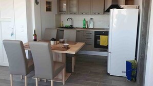 Ett kompakt kök med en matplats, inrett med ett träbord, grå stolar, ett vitt kylskåp och en inbyggd ugn.